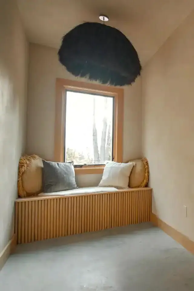 Cozy window seat with slatted wood base and large pendant light in Maine A-frame cabin.