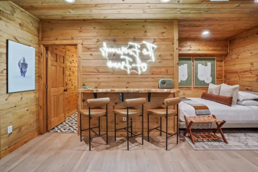 Compact bar and sleeping nook inside a Hocking Hills A Frame Cabin with neon sign and rustic wood finishes.