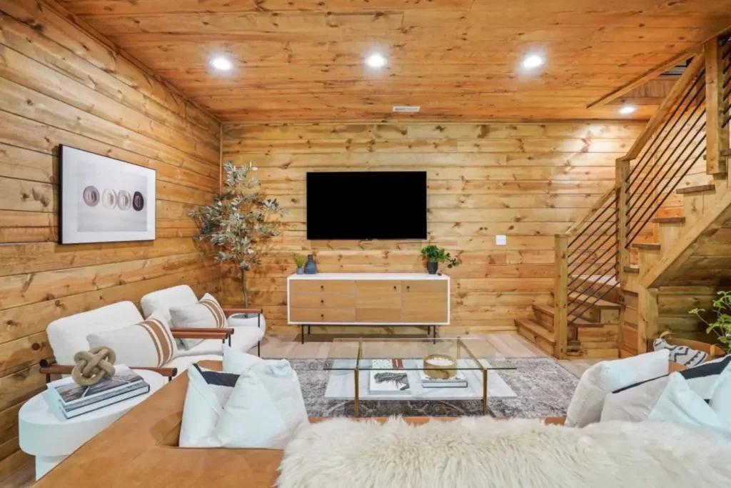 TV lounge area with cozy seating, rug, and staircase against wood walls in a Hocking Hills A Frame Cabin.