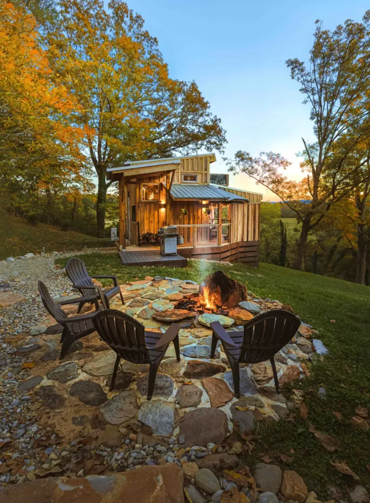 Little River Tiny House in Maryville, Tennessee, featuring a cozy outdoor fire pit area with seating, surrounded by autumn trees at dusk.