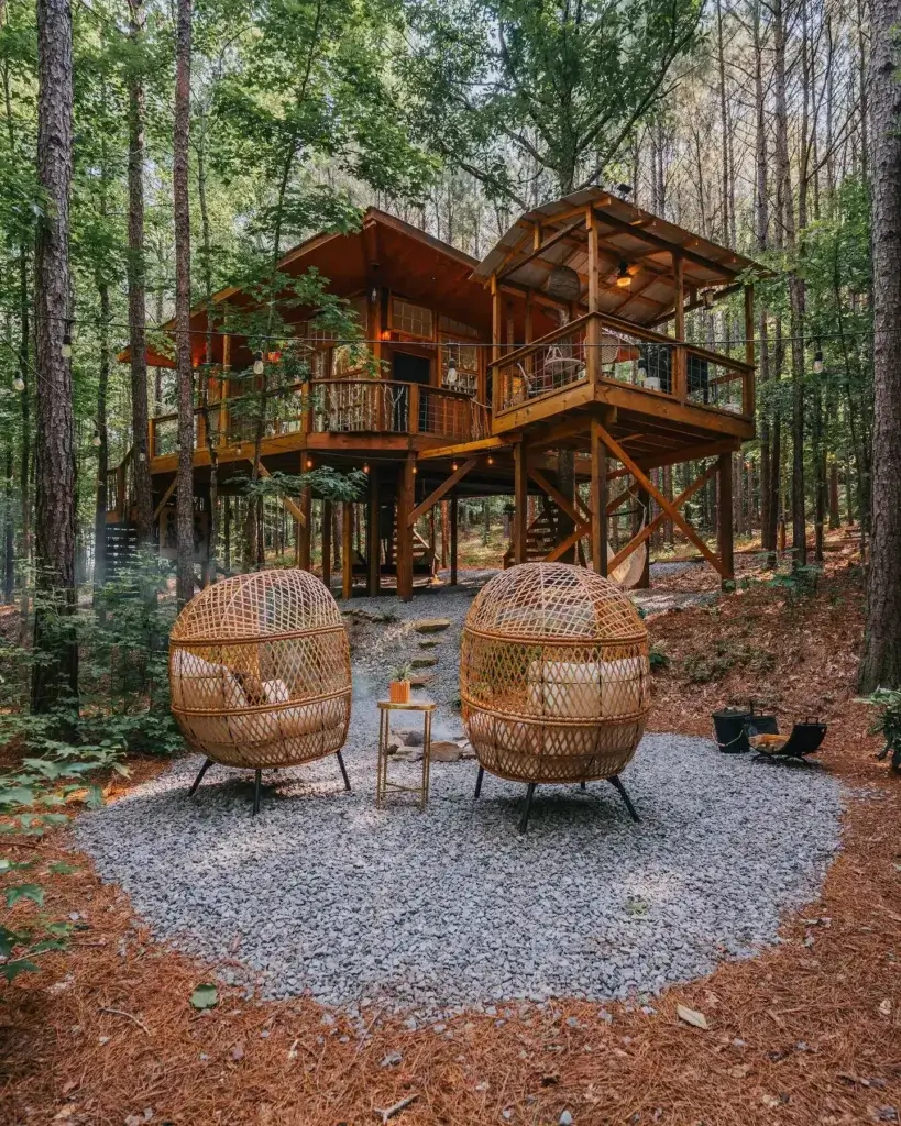 Wanderlust treehouse rental elevated in Alabama forest with cozy wicker chairs on gravel patio below - Firefly Treehouses, Crane Hill