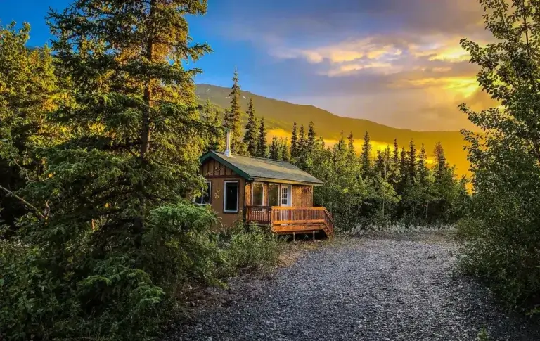 Cozy Glacier Breeze tiny cabin rental nestled in Alaskan forest with dramatic sunset over mountains in Palmer, Alaska