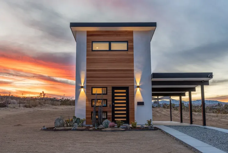 Sleek NeekSleeps 300sqft Tiny House in Joshua Tree, California, with a modern facade of white and wood, set against a vibrant desert sunset.