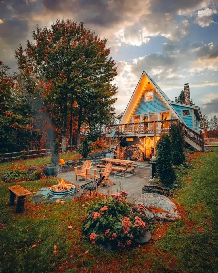 Inviting blue Kingdom A-Frame cabin rental patio with lit fire pit under autumn trees in Burke, Vermont