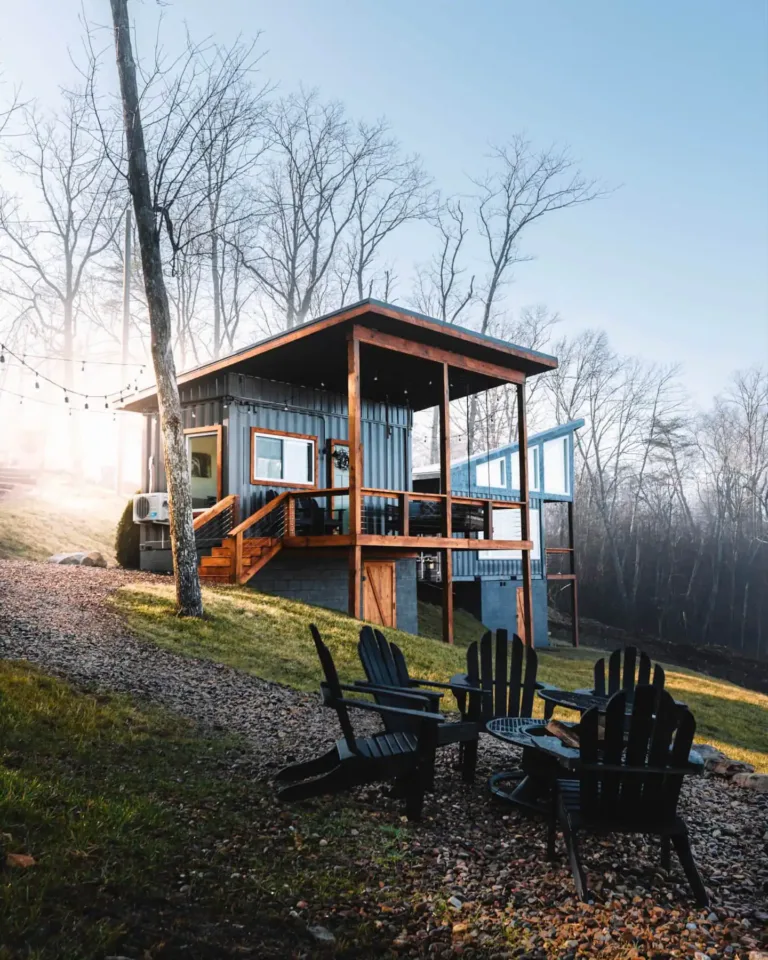 The Belvedere Box, an innovative container tiny home in Rising Fawn, GA, with an elevated deck and outdoor seating overlooking a misty, wooded landscape.