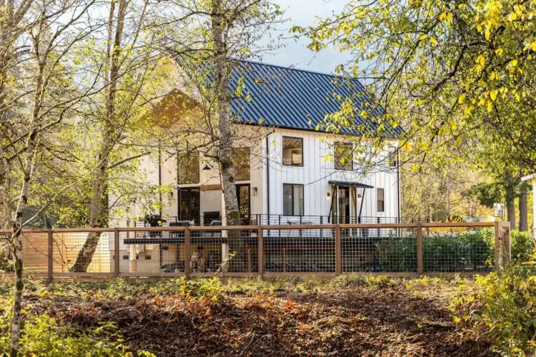 North Bend Modern Farmhouse in Washington, a stylish white guesthouse with dark trim, surrounded by trees and a fenced yard in soft daylight.
