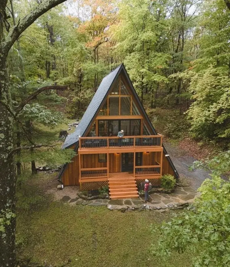 The Upstate A modern A-frame cabin rental with wood siding and balcony nestled in dense New York forest