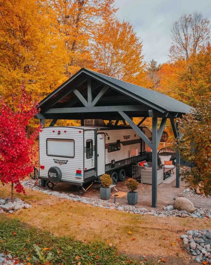 Modern travel trailer glamping site in Remsen, New York, with a covered patio, outdoor lounge, and vibrant autumn foliage.