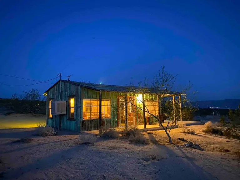 Classic rustic Joshua Tree homestead cabin Airbnb glowing at twilight in the desert