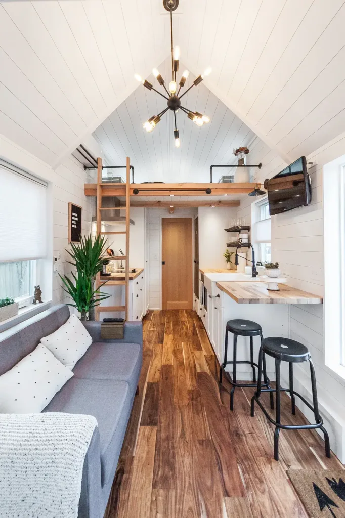 Bright and airy interior of a Unique Modern Tiny House, showcasing a comfortable living area, kitchen counter, and sleeping loft with white shiplap walls and wood floors.