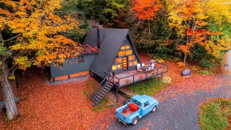 The Summit House A-frame cabin rental surrounded by peak autumn foliage with vintage blue truck in Stowe, Vermont