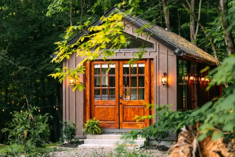 The GLOCABIN in Hocking Hills, Ohio, a woodland cabin with large wooden French doors, surrounded by lush green foliage and soft lighting.