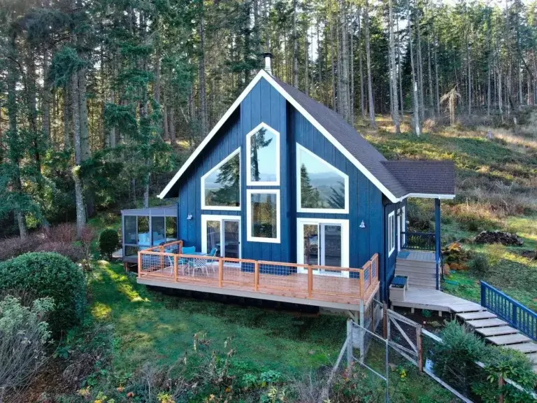 Modern blue Luxurious Getaway House rental with large windows and deck on forested hillside in Eugene, Oregon