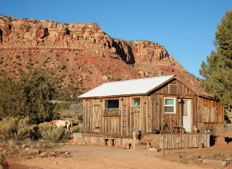 Authentic rustic homesteader cabin rental with weathered wood at the base of red rock cliffs on Arizona ranch