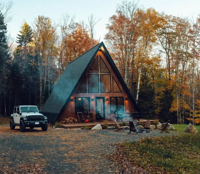 The Chal-A-Frame Vermont A-frame cabin rental with fire pit area and Jeep parked amidst autumn trees near Stratton