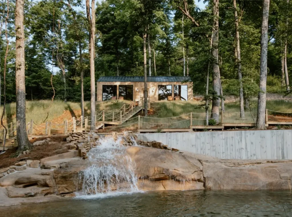 The Cliffs Bungalows in Hocking Hills, with a cabin nestled on a slope overlooking a man-made waterfall and pool, surrounded by forest.