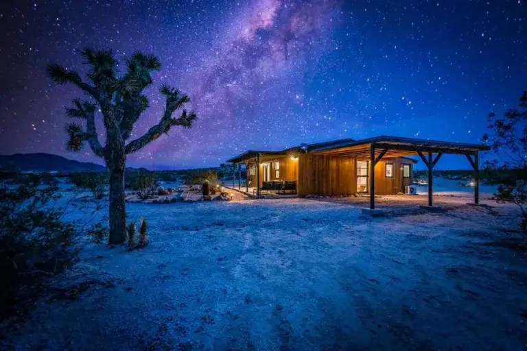 Jackalope Cabin rental glowing under spectacular Milky Way night sky in Joshua Tree desert, California