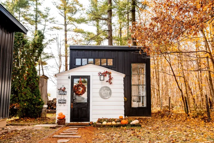 The Tiny Shed Country Escape in Fort Wayne, IN, a creatively designed tiny home with a white facade and black accents, decorated with pumpkins and wreaths for fall.