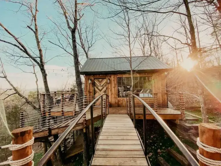 Suspension bridge leading to Mountaintop Luxury Treehouse rental at Selah Ridge against bright sun, Ringgold, Georgia