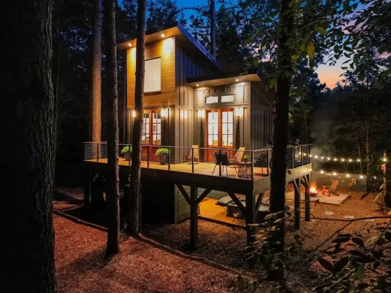 Modern Gigi's Treehouse rental lit up at night with deck and fire pit area in Huntersville, North Carolina