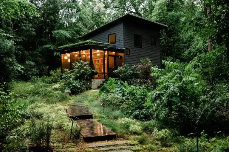 Secluded modern tiny house rental with glowing screened-in porch surrounded by lush greenery in Durham, NC