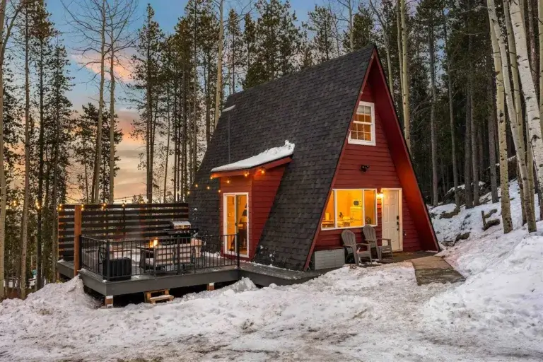 Vibrant red Hidden Ruby A-frame cabin rental with deck surrounded by snowy Colorado mountain forest in Evergreen
