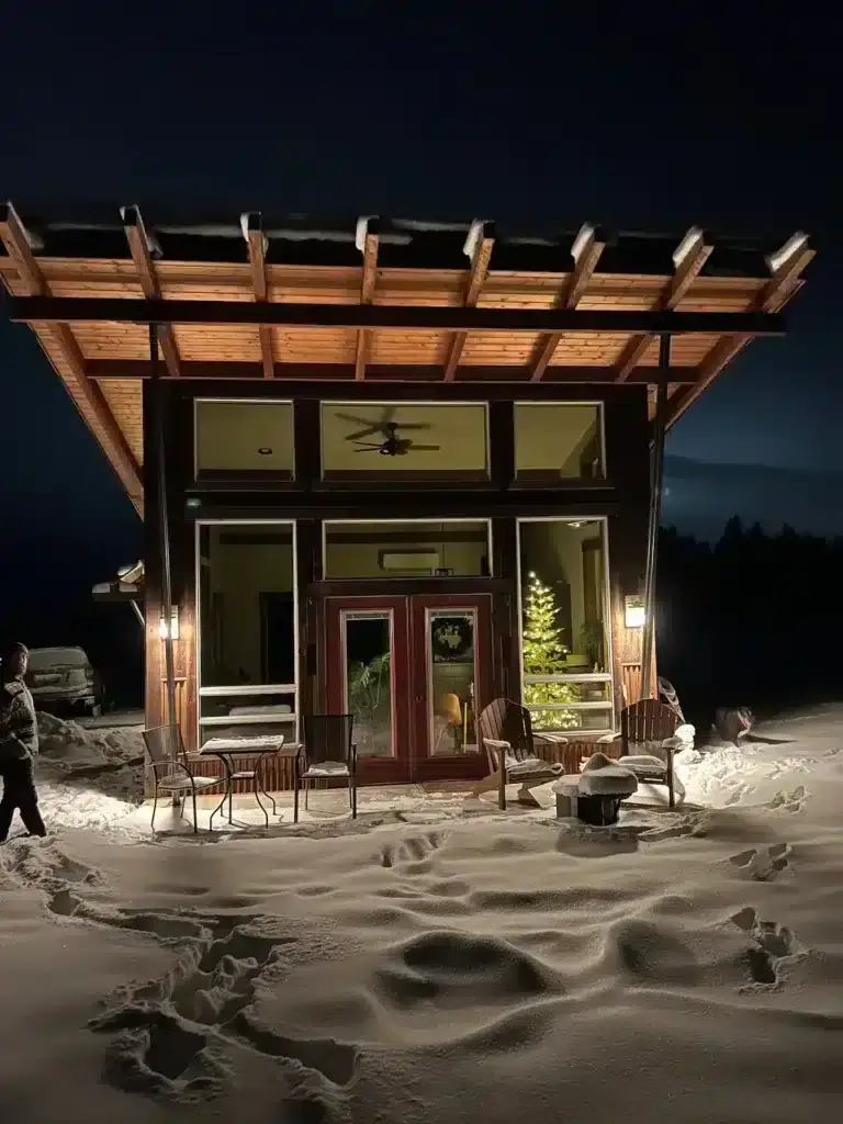 Modern Calowahcan cabin rental with lit overhanging roof and glass front surrounded by deep snow in Ronan, Montana