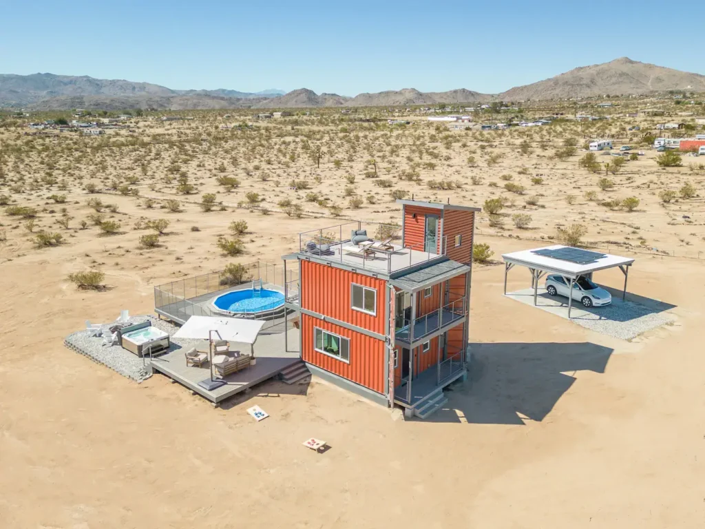 The Joshua Tree Block Tower's shipping container home design, featuring vibrant orange vertical stacking, a pool, and rooftop deck in a desert setting.
