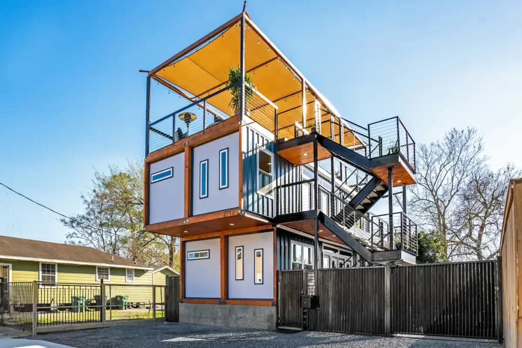 Innovative urban shipping container home design in Houston, featuring a multi-level structure, extensive outdoor decks with canopies, and modern industrial lines.