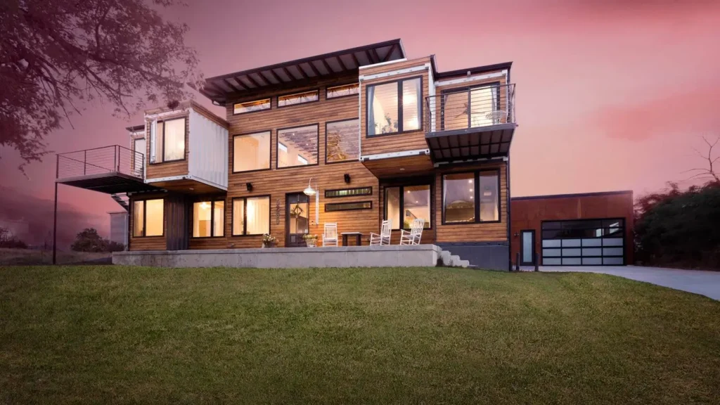 Design of a spacious Denver shipping container home, showcasing warm wood cladding, multiple balconies, and extensive windows illuminated against a sunset sky.