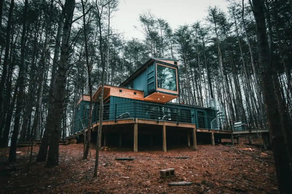 Architectural design of The Box Hop in Hocking Hills, a dark shipping container home with dramatic cantilevered sections and a wooden deck deeply integrated into a forest.