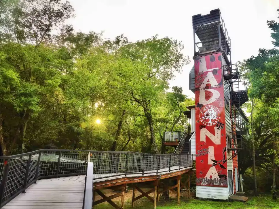 The Air Castle Treehouse, a tall shipping container home design in Ladonia, TX, featuring a striking vertical 'LADONIA' mural and multiple elevated living spaces.