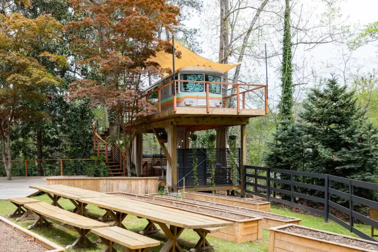 Unique Airstream treehouse rental in East Point Georgia, featuring a vintage trailer on an elevated platform with a yellow awning and picnic area.