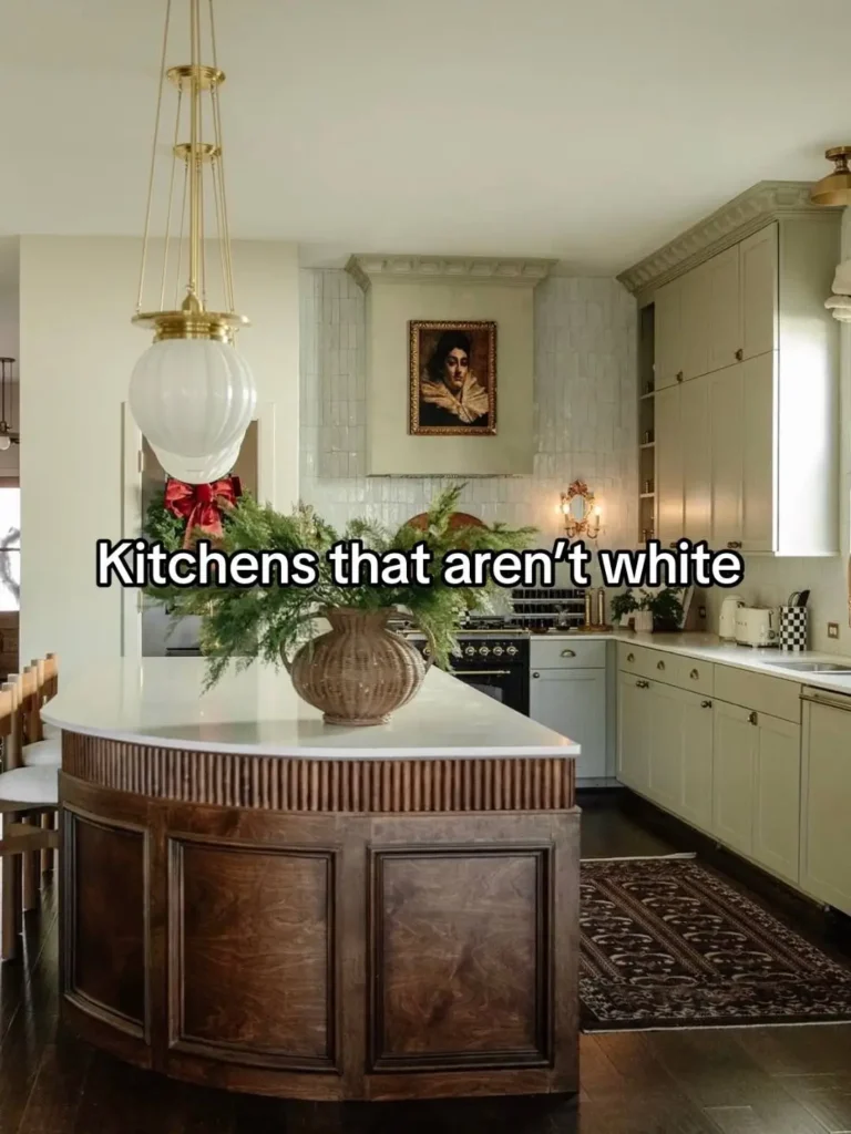 Chic 2025 kitchen showcasing the move beyond white, with elegant sage green cabinetry, a contrasting dark wood reeded island, statement pendant light, and curated artwork creating a sophisticated space.