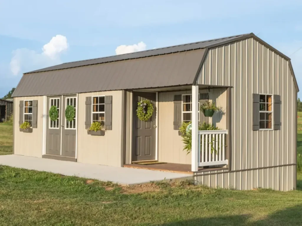A high barn lofted tiny home shell with beige metal siding, a brown roof, and a small front porch, ready for interior finishing.