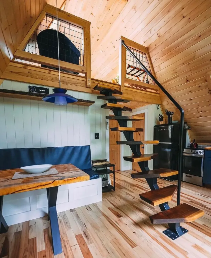 Modern A-frame loft stairs with light wood treads and metal supports in a simple tiny house interior.