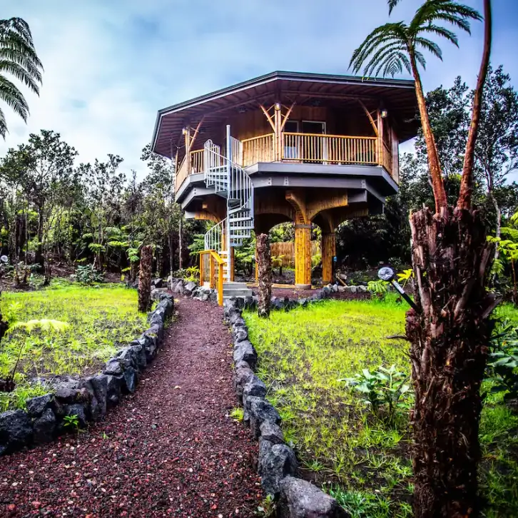 Octagonal Bamboo Treehouse rental in Volcano Hawaii, with distinctive bamboo posts, white spiral staircase, and lush tropical garden path.