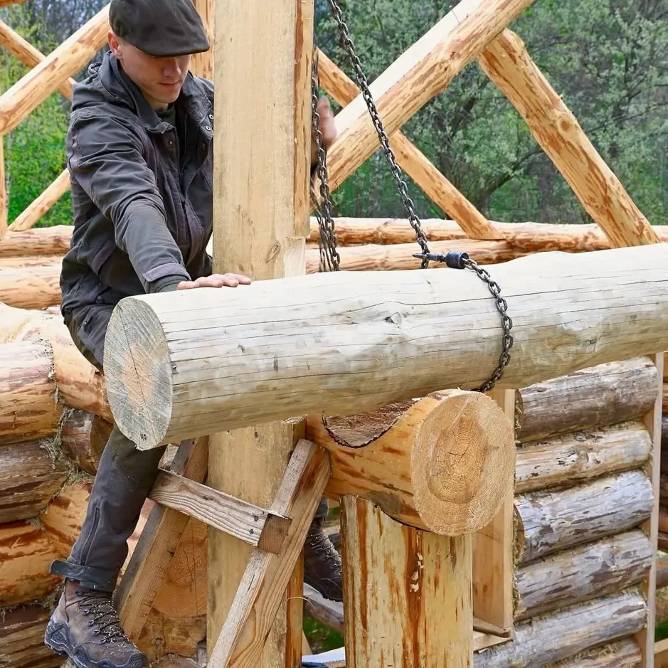 A close-up of a log home builder guiding a large log with a chain to fit it perfectly into the saddle notch of the log below.