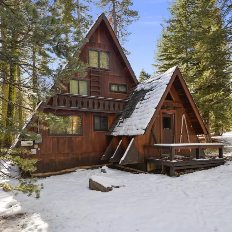 A classic wood-paneled Tahoe A-frame cabin in Alpine Meadows, set in a snowy forest under a clear blue sky, perfect for a ski getaway.