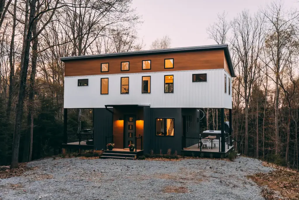The Rohe Block, a Hocking Hills shipping container home design, featuring an architecturally unique 'floating' white upper level with wood trim over a dark base.
