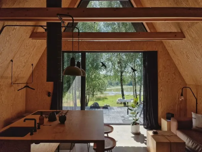Modern minimalist A-frame cabin ('Minimalisticka chata') interior with kitchen island and lakeside view.