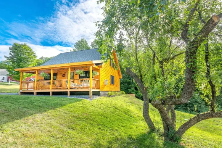 The Bradley log cabin kit on a lush green hill with a fully furnished covered porch.