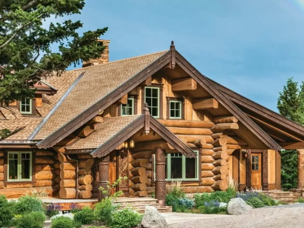 A stunning handcrafted log home with intricate woodwork, surrounded by landscaping, with a rainbow in the sky.