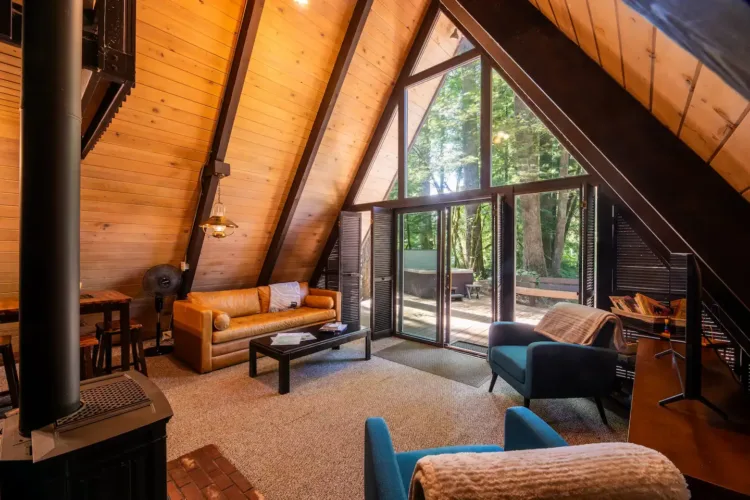 Spacious simple A-frame house interior ('Sky Haus') with high wood ceilings, large windows, and teal accent chairs.