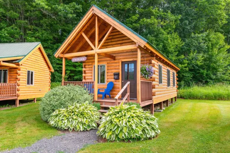 A classic chalet-style two-bedroom log cabin kit with a loft and beautiful summer landscaping.