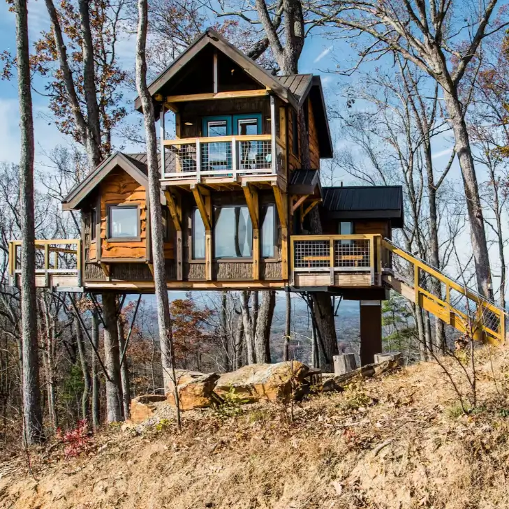 Multi-level rustic wooden Sanctuary treehouse rental by Earth & Sky Dwellings in Asheville North Carolina, nestled in autumn forest with large windows.