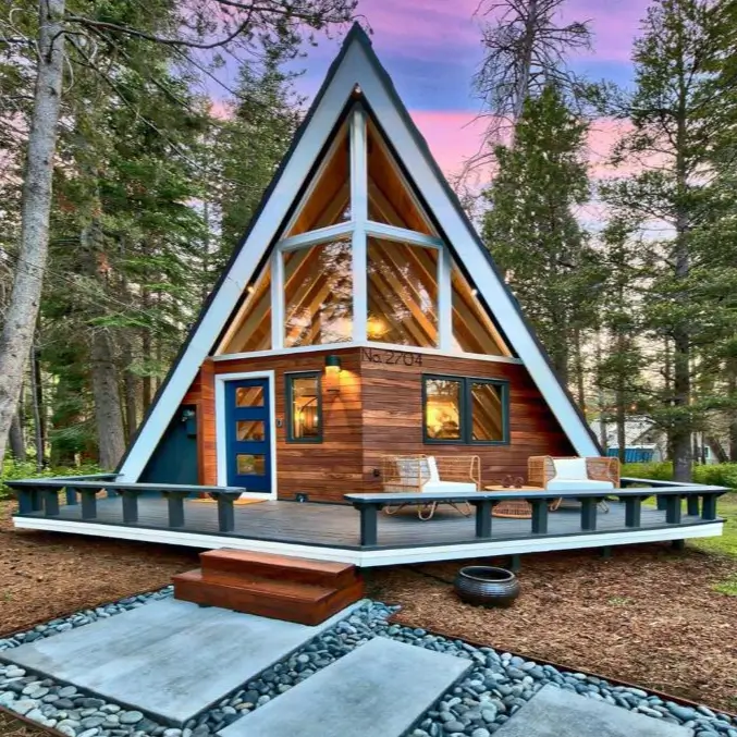 The stunning Luxury A-frame LX04, a modern Tahoe A-frame cabin in South Lake Tahoe, featuring a wraparound deck and stylish design, pictured at sunset in the woods.