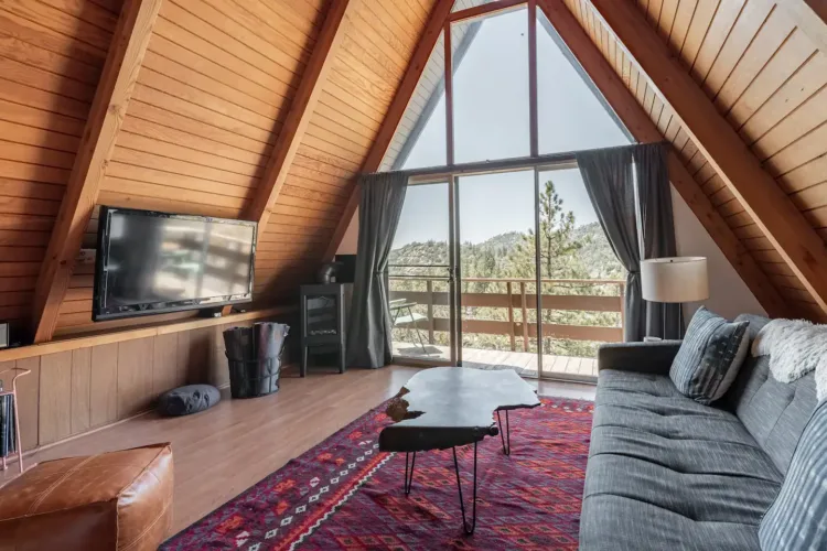 Classic A-frame cabin interior (Lake Arrowhead) with wood paneling, dark sofa, and vibrant red patterned rug.