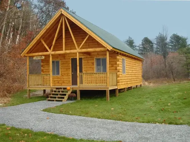 The large Lakeview log cabin kit with a welcoming gravel path and decorative pumpkins on the steps.