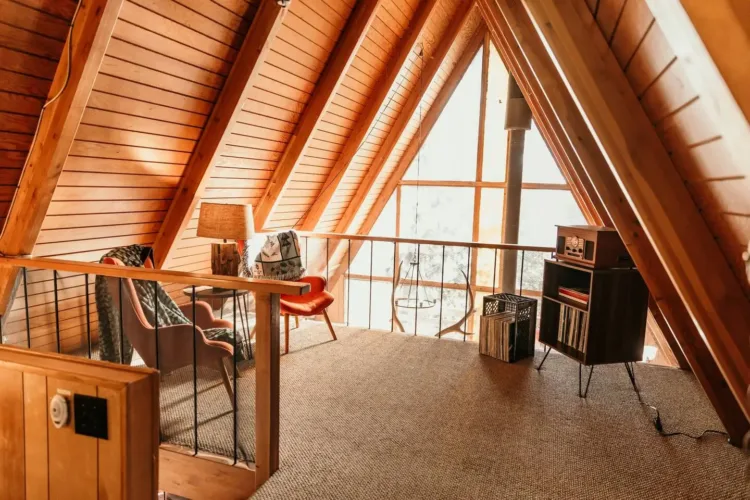 Cozy A-frame house interior loft used as a retro listening nook with record player and view from triangular window.